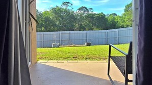 A covered patio with a view of a fenced yard and a clear sky.