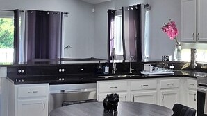 A modern kitchen with a round dining table, black chairs, white cabinets, and a ceiling fan.