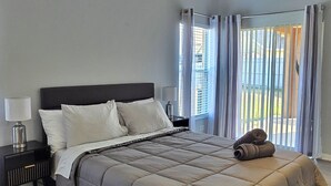 A bedroom with a bed, a nightstand, a ceiling fan, and a window with curtains.
