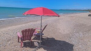 Une plage avec un parasol rouge, une chaise rouge et une table.