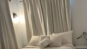 A neatly made bed with a white comforter and pillows, a bedside table with drawers, and a wall-mounted light fixture. - Peaceful Villa near beaches to enjoy El Poblado de Boqueron. Pet-Fiendly. (Boquerón)