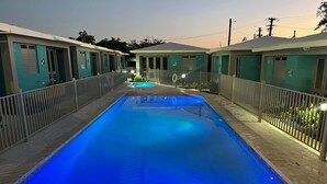 A swimming pool with a tiled border, surrounded by a fence and adjacent to a row of motel-style buildings. - Peaceful Villa near beaches to enjoy El Poblado de Boqueron. Pet-Fiendly. (Boquerón)