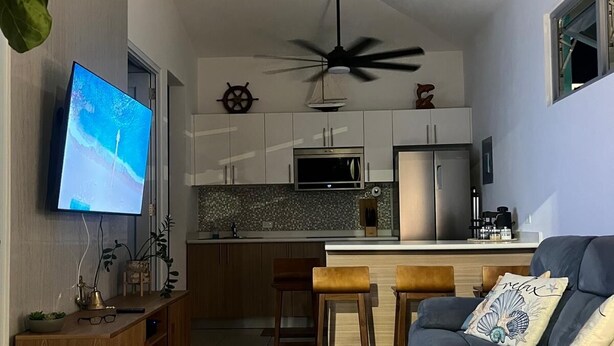 A modern kitchen with a central island, a dining area with bar stools, a flat-screen TV, and a ceiling fan. - Peaceful Villa near beaches to enjoy El Poblado de Boqueron. Pet-Fiendly. (Boquerón)