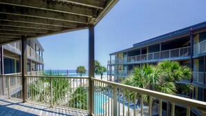 A wooden deck with a pool and palm trees, overlooking a beach and a multi-story building with balconies. - 2BR Beachside retreat, sleeps 6, walk to beach! (Gulf Shores)