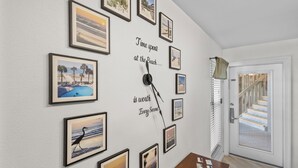 A wall with multiple framed beach photographs and a clock with the phrase "Time spent at the beach is worth every second." - 2BR Beachside retreat, sleeps 6, walk to beach! (Gulf Shores)