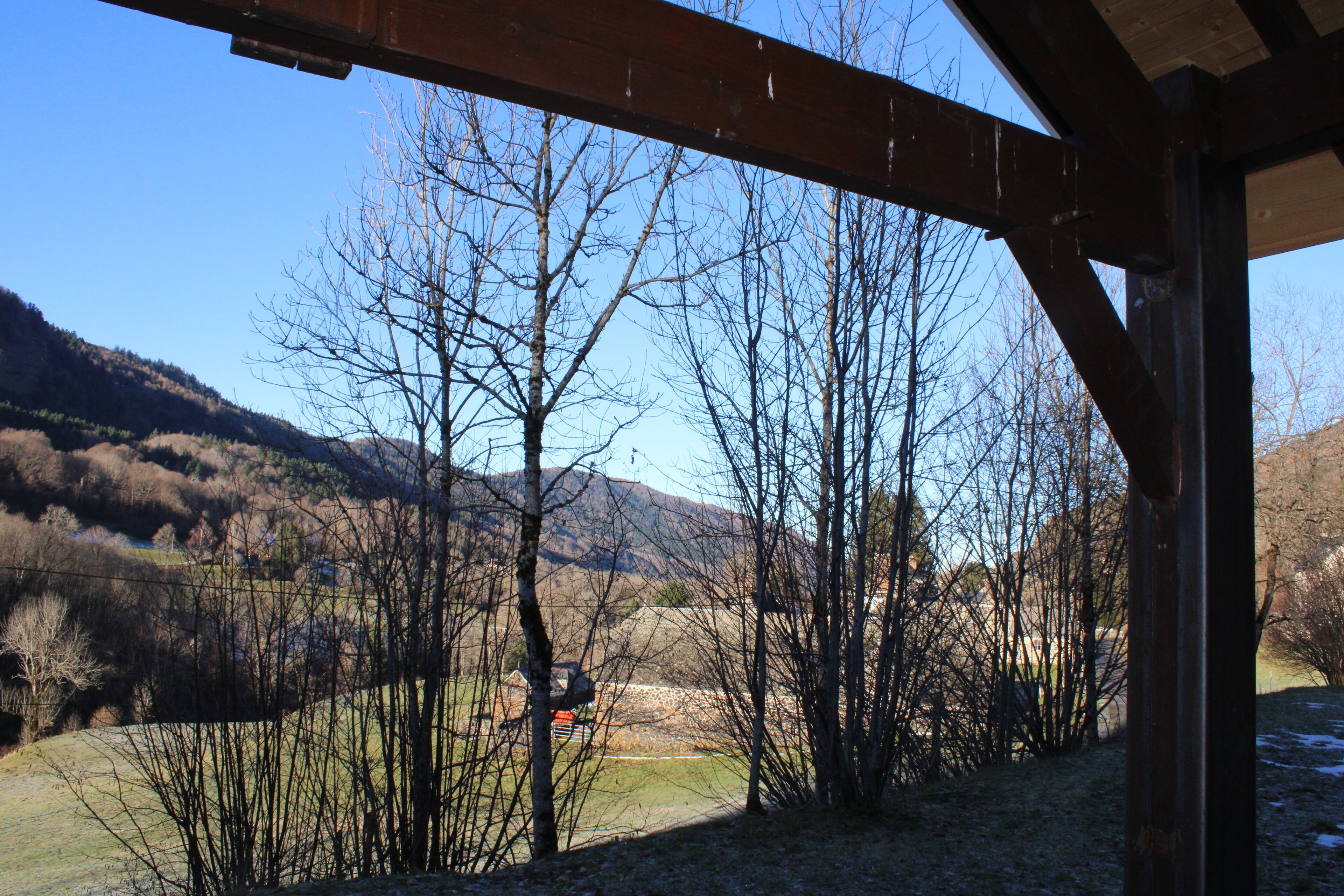 A rustic wooden structure with a view of a mountainous landscape and leafless trees.