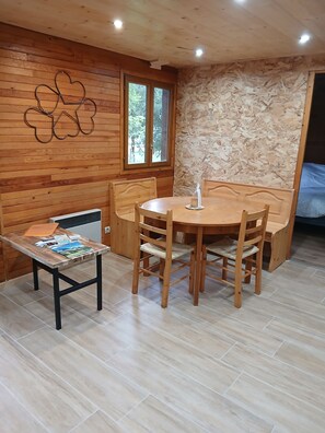 Un coin repas accueillant avec une table et des chaises en bois, une petite table d’appoint avec des magazines et une fenêtre donnant sur les arbres.