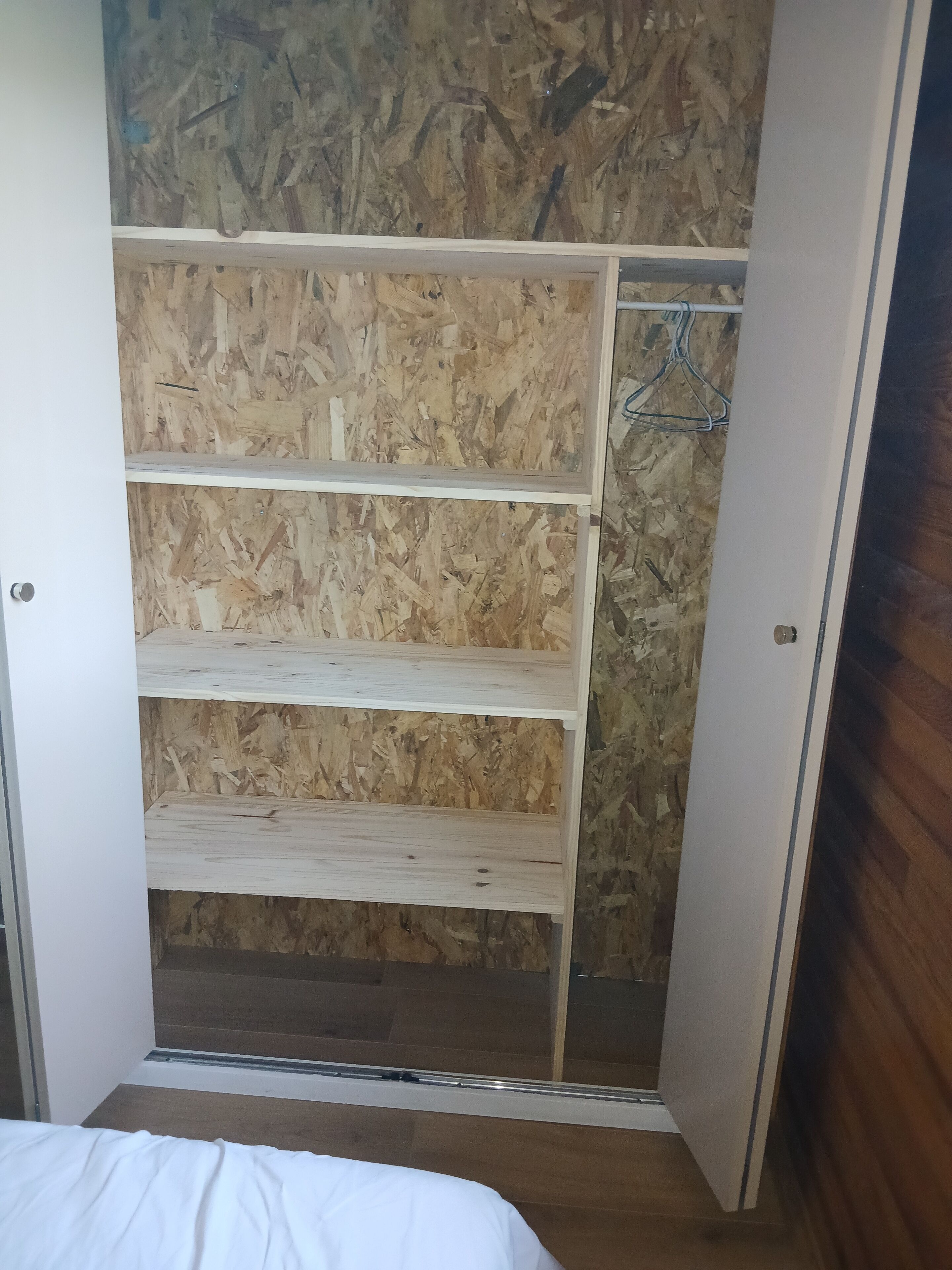 A room with a built-in wardrobe featuring three wooden shelves and a hanging rod.
