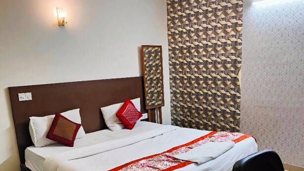 Een net opgemaakt bed met hoofdbord, een rode en witte plaid en een zwarte stoel in een hotelkamer.