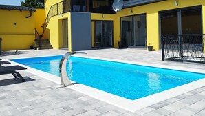 Un edificio amarillo de dos pisos con piscina, ventanas amplias y una antena parabólica.