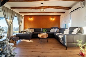 Relax in this inviting living room with a large L-shaped sofa, a round coffee table, and a high ceiling with exposed beams.