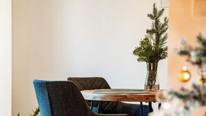 Un comedor con una mesa de madera, dos sillas tapizadas, una pequeña planta en maceta y un árbol de Navidad.