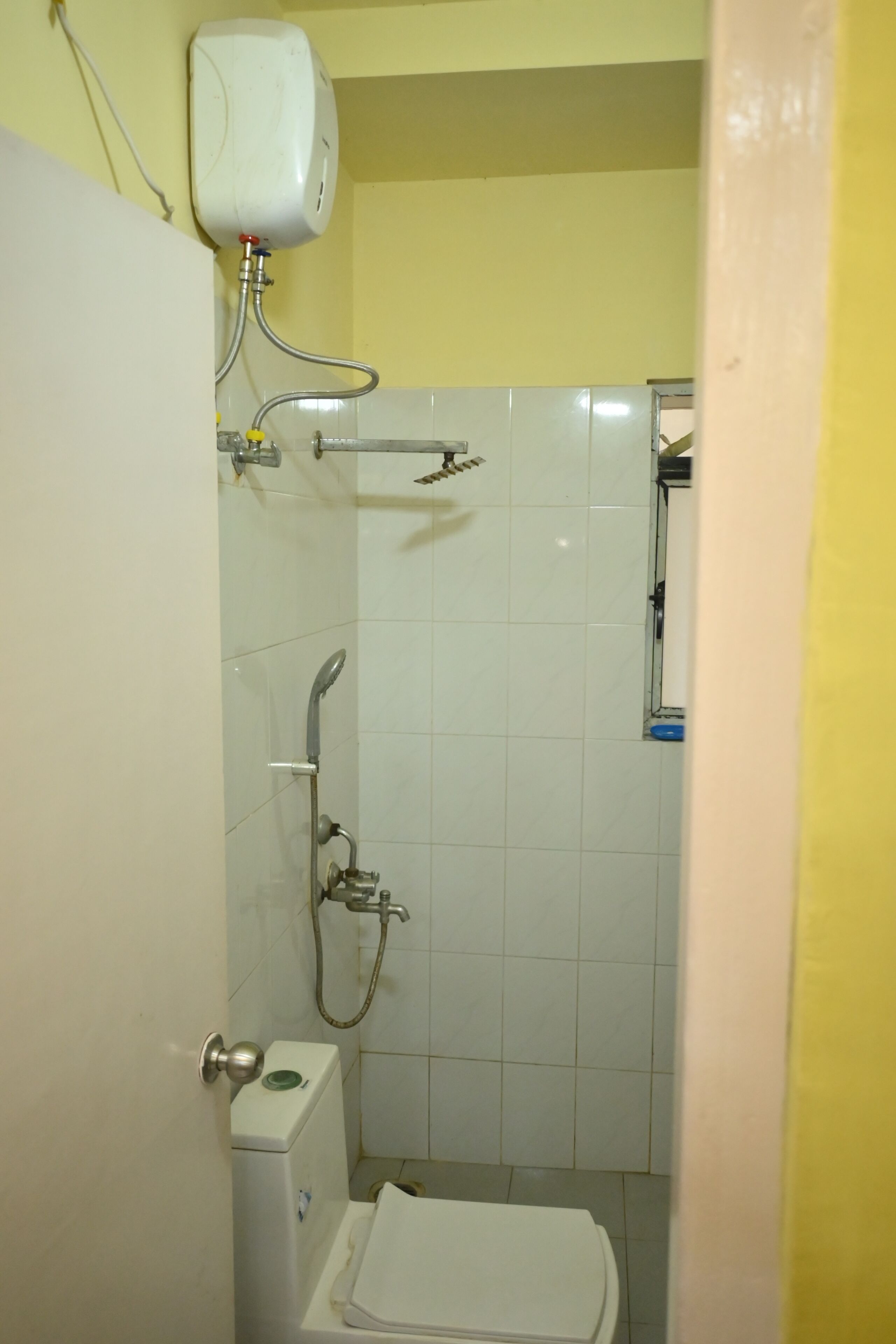 A small, enclosed bathroom with a toilet, a shower, and a wall-mounted soap dispenser.