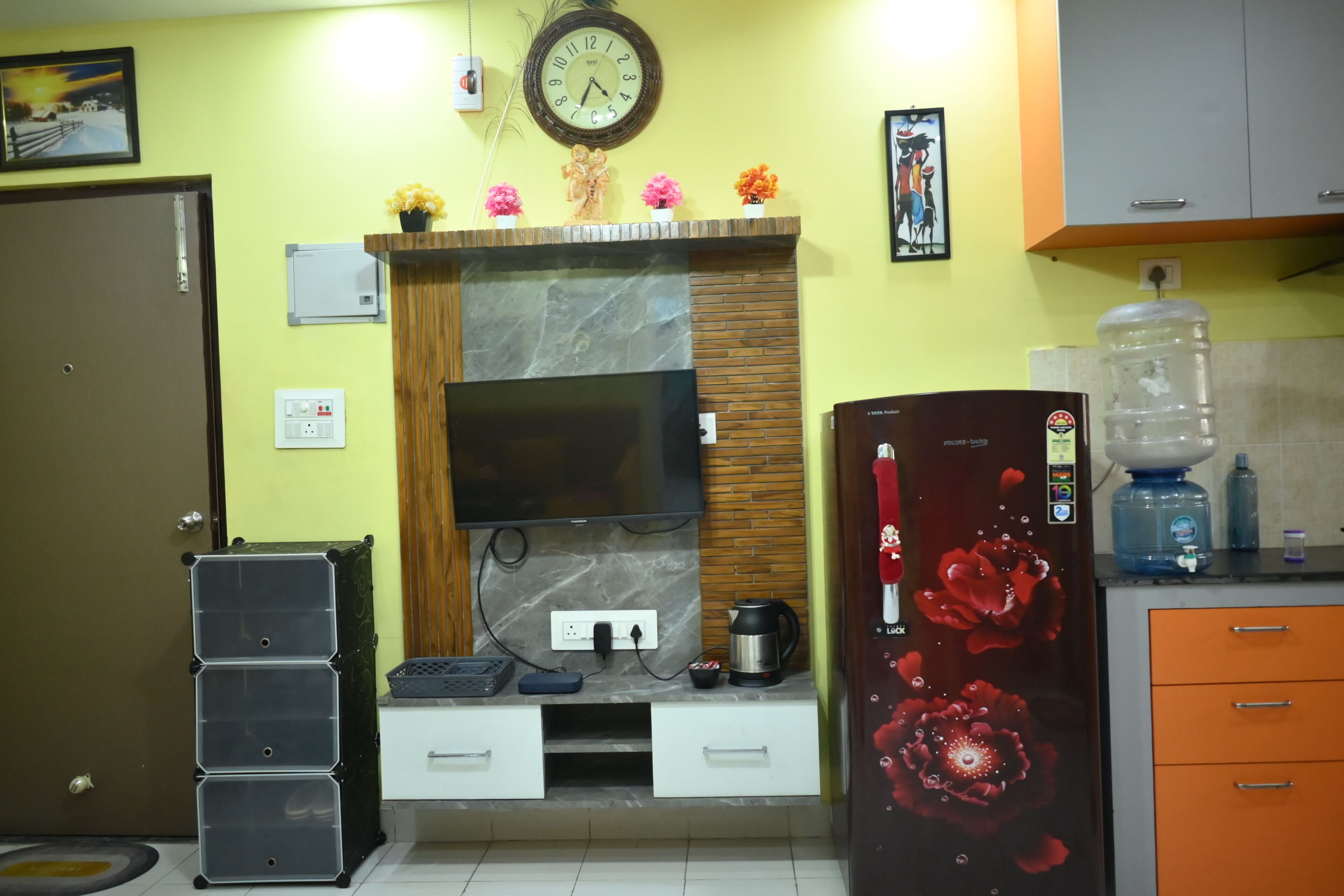 Una cocina con televisor integrado, un reloj, dispensador de agua y un refrigerador con diseño floral.