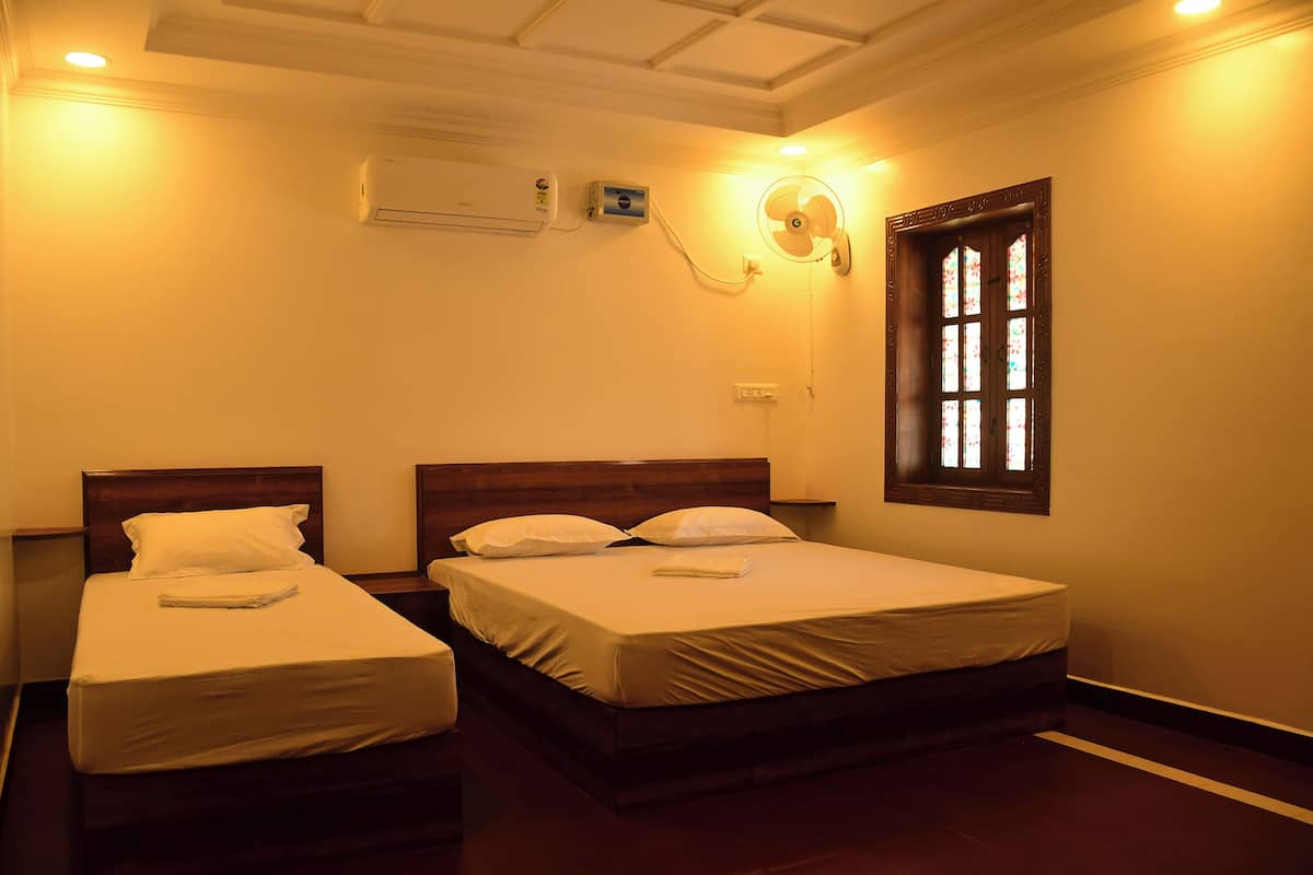 Habitación de hotel con dos camas individuales, ventilador de techo, equipo de aire acondicionado y una ventana con vidrieras.