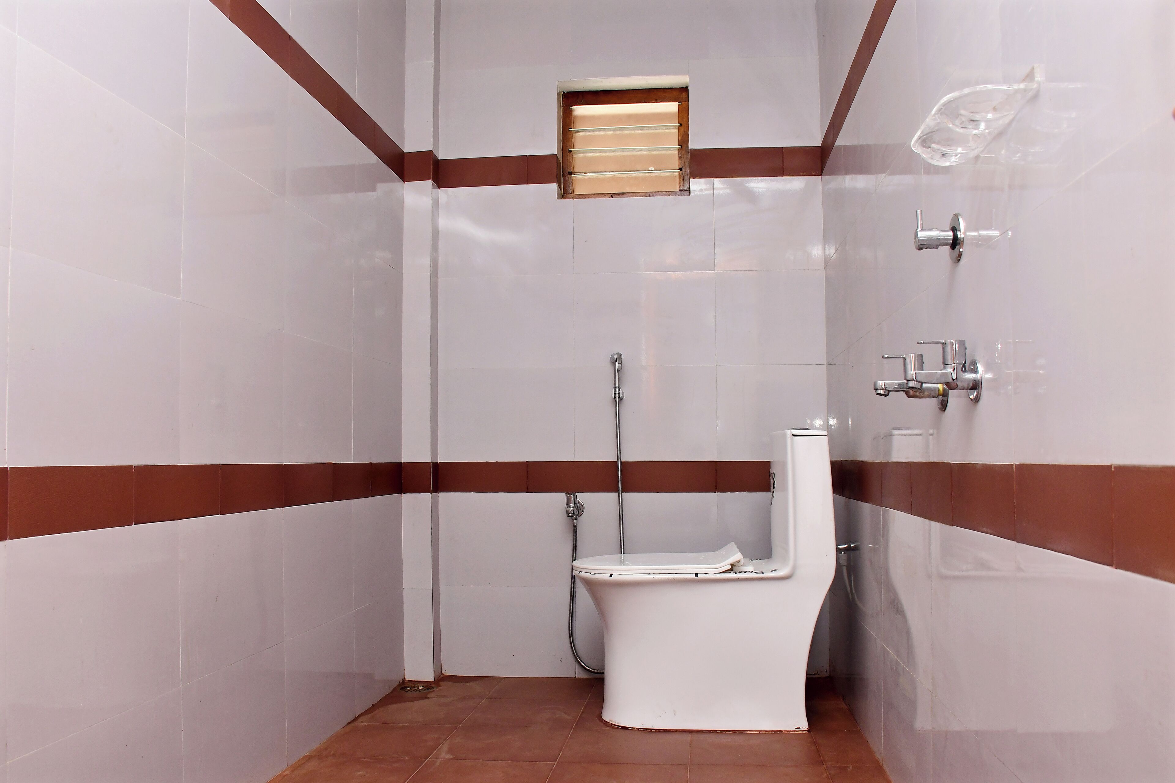 A small, tiled bathroom with a toilet, a shower, and a small window.