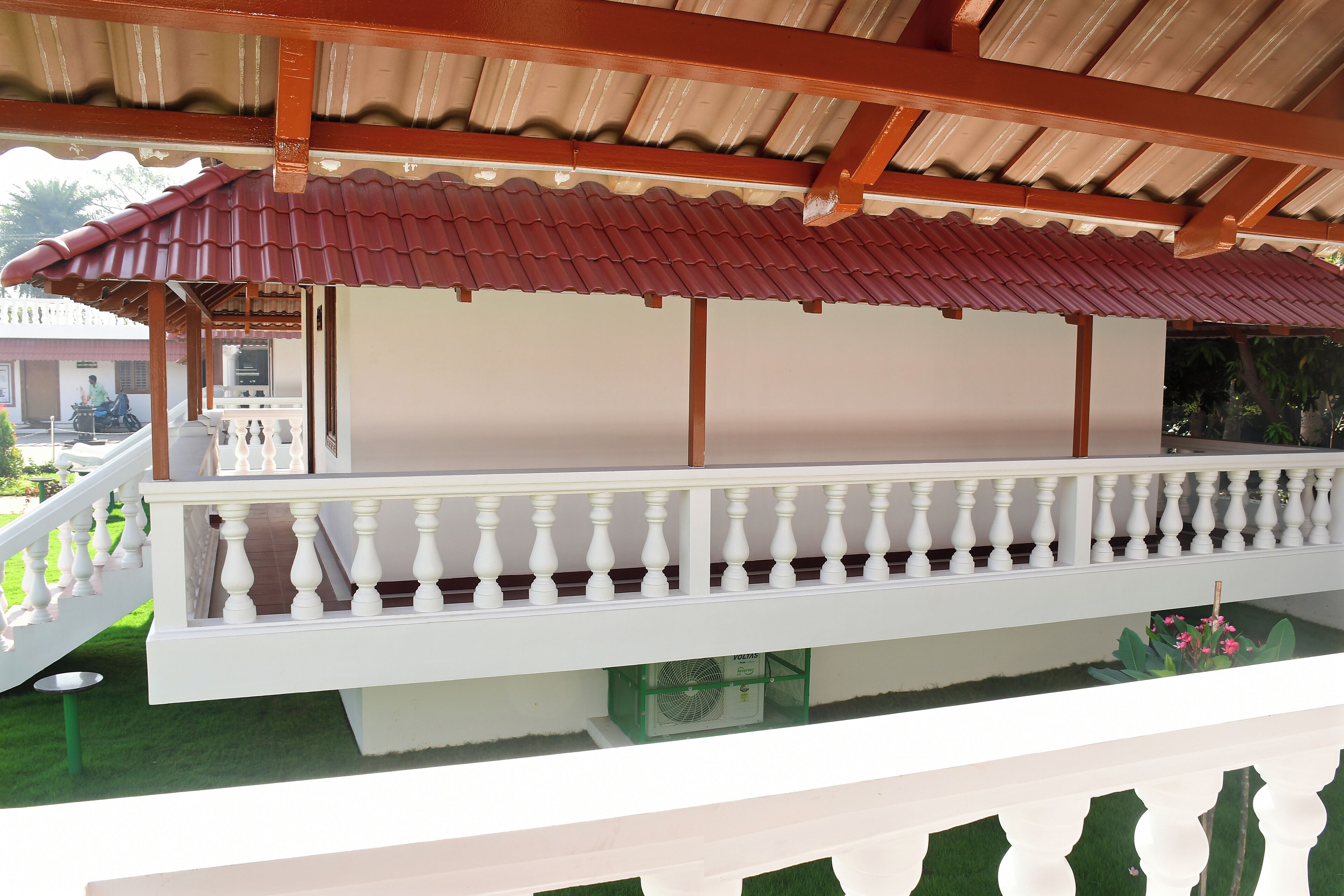 A covered balcony with a white balustrade, a tiled roof, and a view of a building in the background.