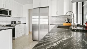 A modern kitchen with white cabinets, a stainless steel refrigerator, a microwave, and a granite countertop. - Private pool home near downtown & beach (West Palm Beach)