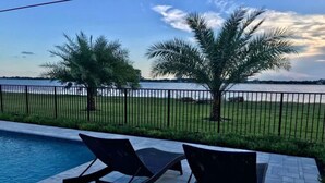A poolside area with two lounge chairs facing a body of water, surrounded by a fence and palm trees. - Private pool home near downtown & beach (West Palm Beach)