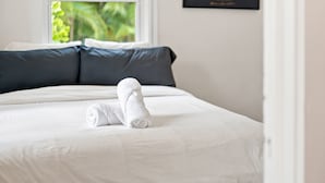Una cama bien hecha con una toalla blanca enrollada, almohadas azul oscuro y un certificado enmarcado en la pared.