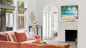 Una sala de estar con chimenea, un sofá y un cuadro de una escena de playa.