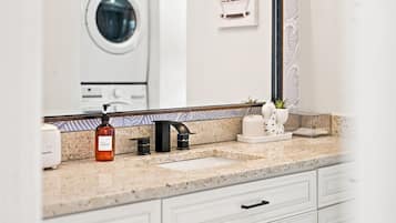 A bathroom with a granite countertop, a black faucet, a soap dispenser, and a mirror reflecting a washing machine.