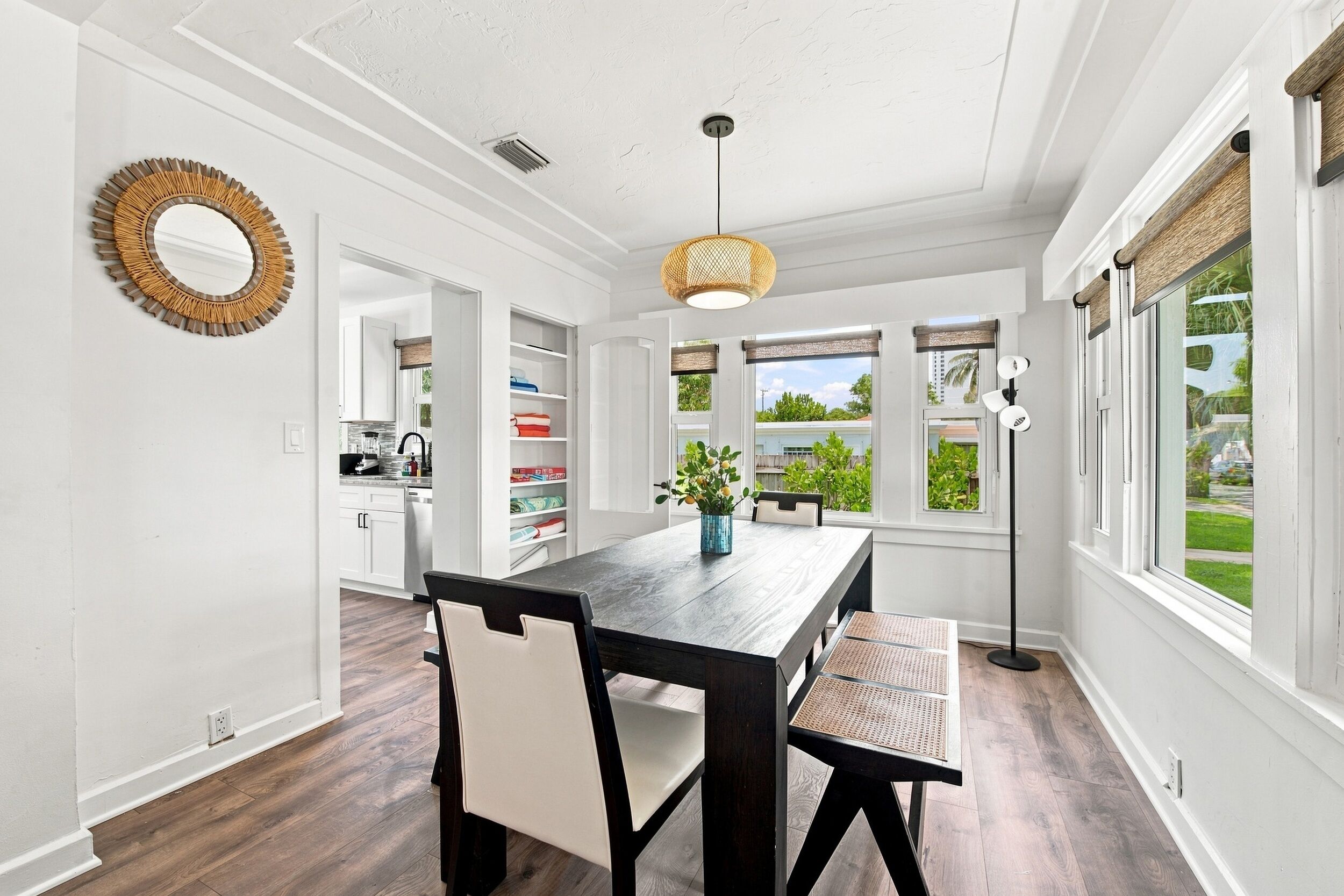 A dining area with a wooden table, chairs, a hanging light fixture, and a view of the outdoors through large windows.