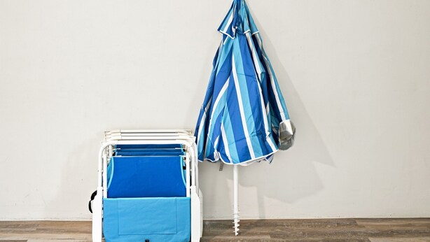 Una habitación con una pared blanca, un paraguas azul y blanco a rayas y una cuna portátil blanca con colchón azul.