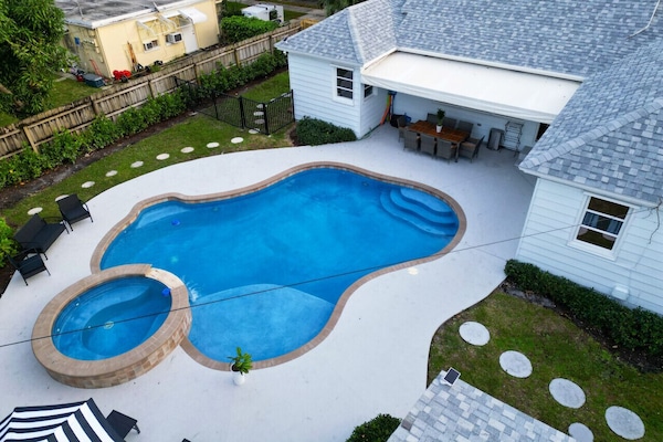 Aerial view showcases a beautiful backyard with a uniquely shaped swimming pool, a spa, and a covered patio area.