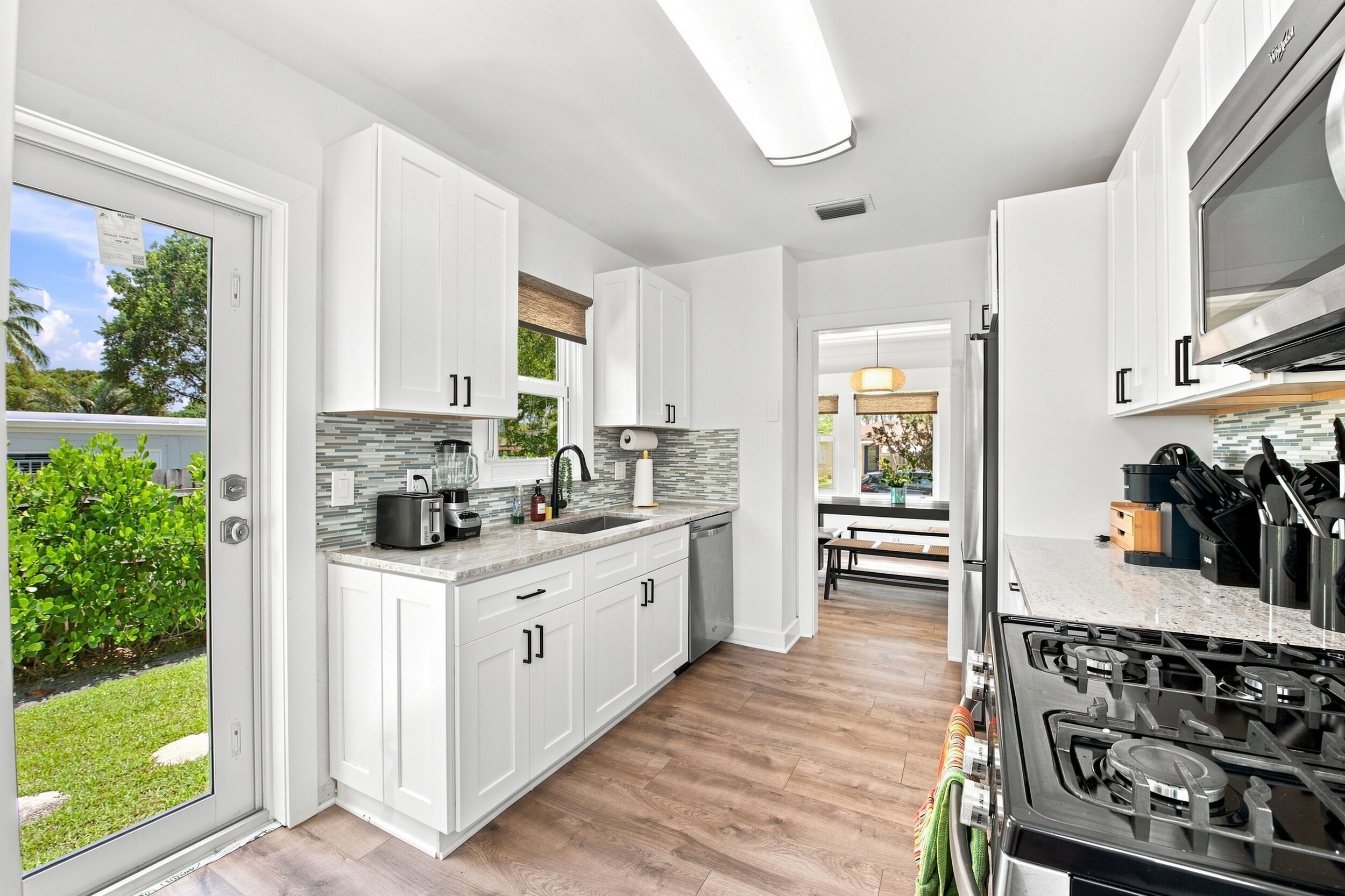 Une cuisine moderne avec des meubles blancs, une cuisinière encastrée et une grande fenêtre.