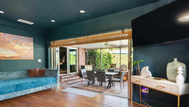 A spacious living area with a blue sofa, a dining table with chairs, and a TV on a black stand. - Pool Home w/ Game Room | Near Peanut Island (West Palm Beach)