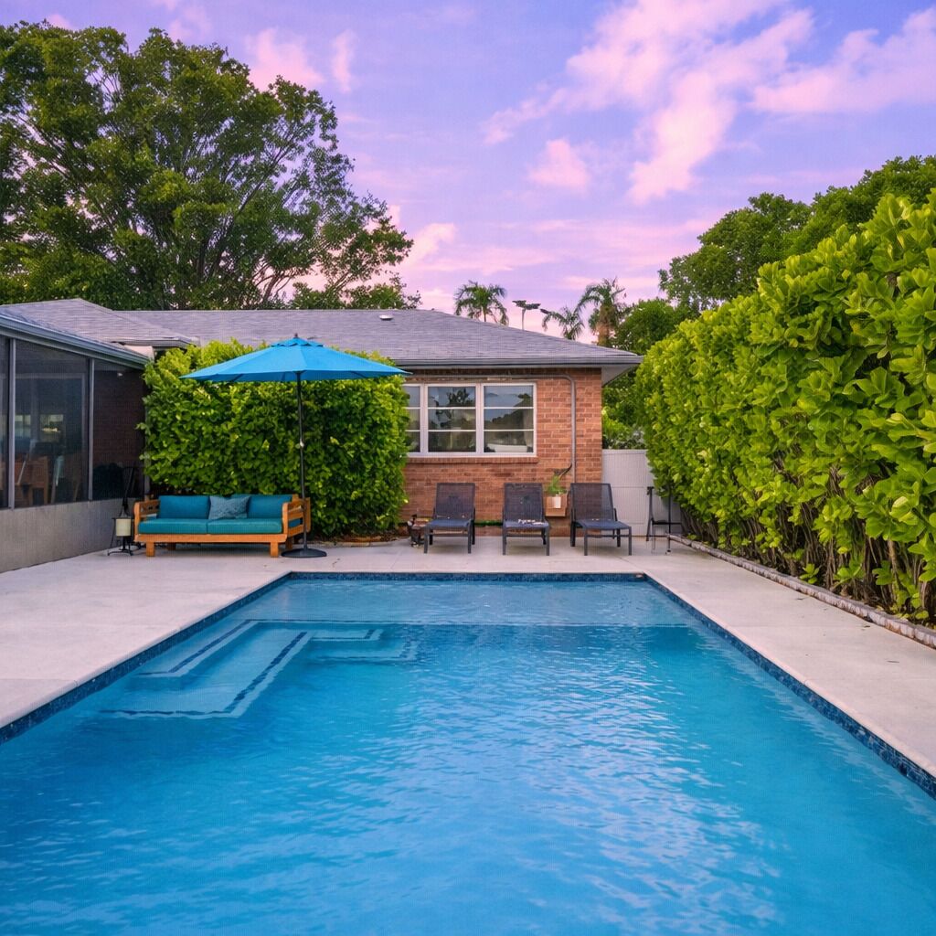 Inviting backyard showcases a sparkling blue swimming pool surrounded by a paved area and lush green landscaping under a clear sky.
