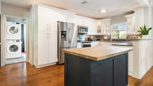 A modern kitchen with white cabinetry, stainless steel appliances, and a wooden island. - Pool Home w/ Game Room | Near Peanut Island (West Palm Beach)