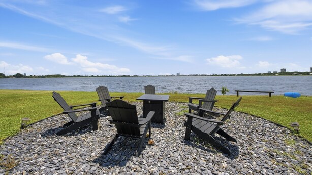 Een terras met Adirondack-stoelen en een tafel, met uitzicht op een waterpartij en een verre stadshemel.