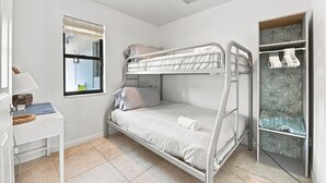 Een slaapkamer met stapelbed, bureau, raam en een kledingkast.