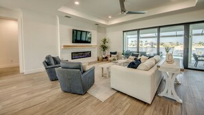 Amplia sala de estar con televisor grande, asientos cómodos, ventilador de techo y vistas a través de amplias ventanas.