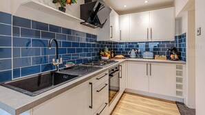 Una cocina moderna con azulejos azules, armarios blancos, un lavabo negro y un horno empotrado.