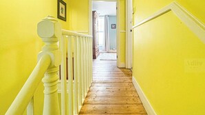 Un pasillo con paredes amarillas y piso de madera, que conduce a una puerta al final.
