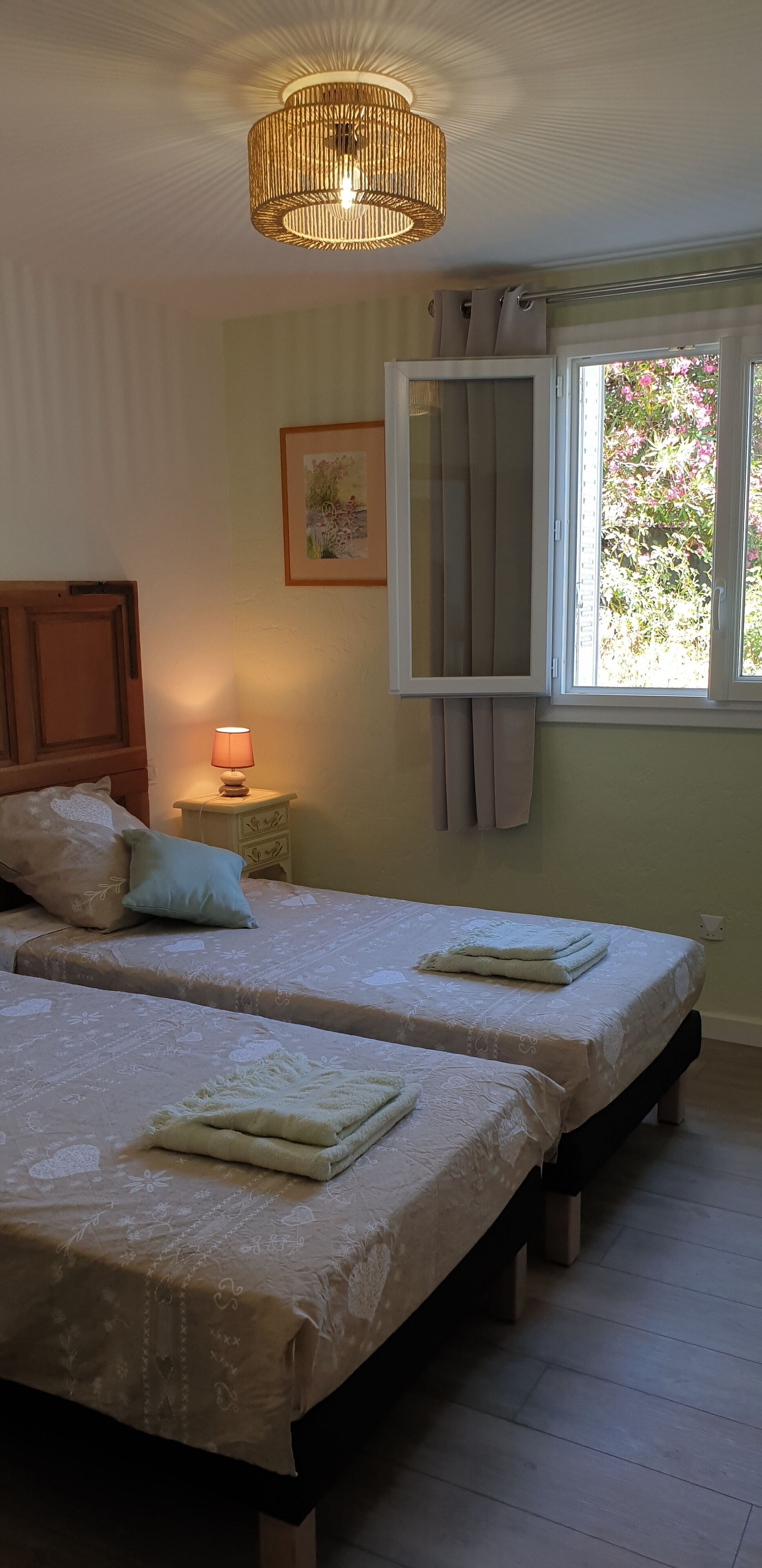 Une chambre avec deux lits, une table de chevet avec une lampe, une fenêtre avec des rideaux et un luminaire suspendu.