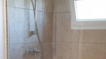 Una ducha con puerta de cristal, una ventana arriba y una encimera blanca a la izquierda.
