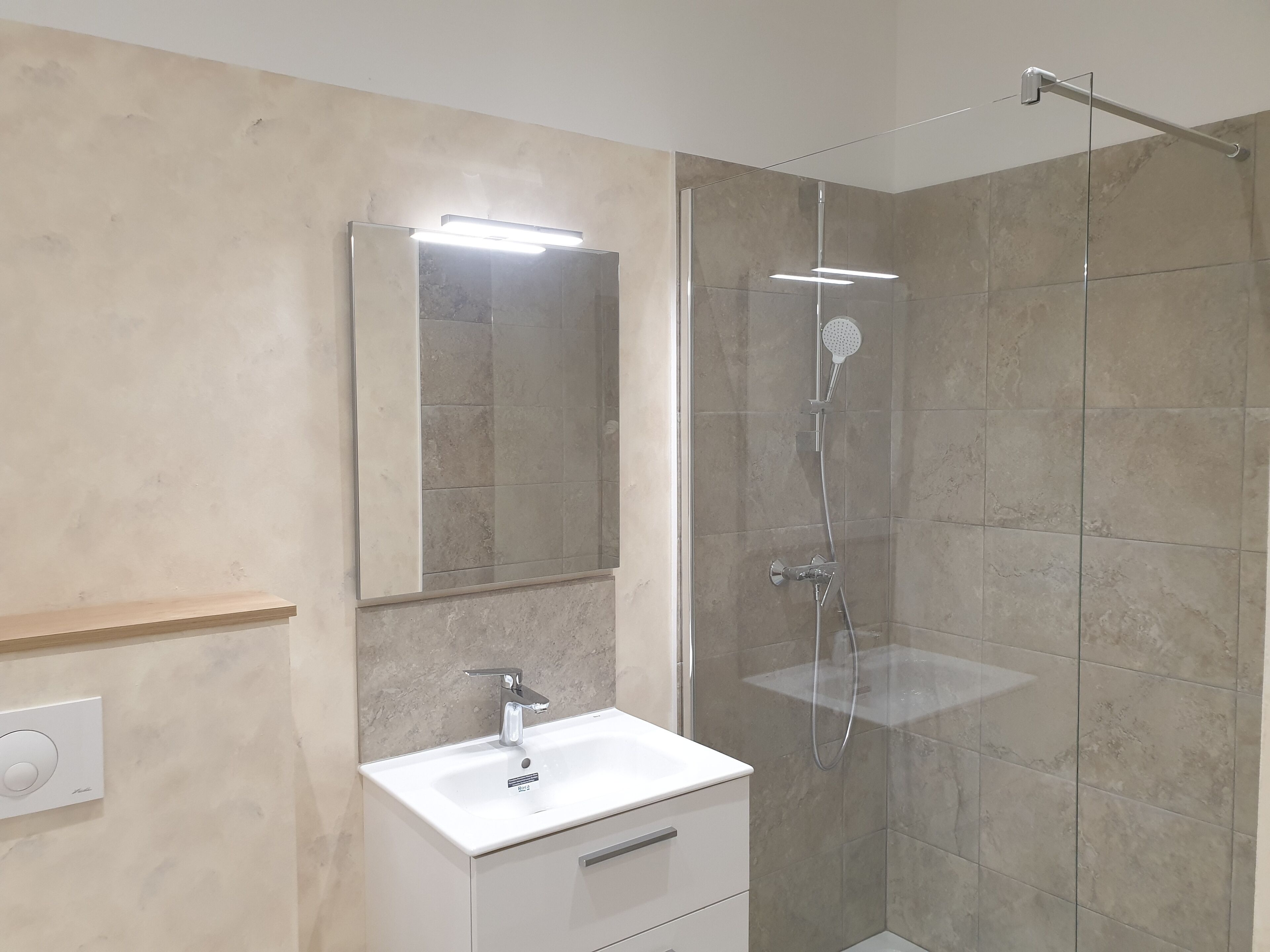 A modern bathroom with a glass-enclosed shower, a white sink, and a mirror with integrated lighting.