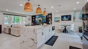 A modern kitchen with a marble island, pendant lights, and a dining area with white chairs.