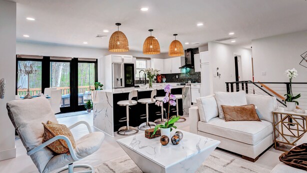 A modern living room with a white sofa, a coffee table, and a dining area with bar stools.