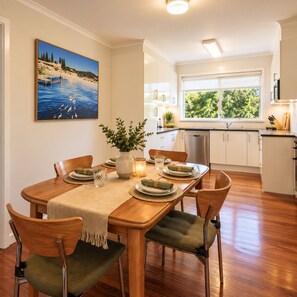 A dining area with a wooden table, chairs, and a painting of a beach scene.