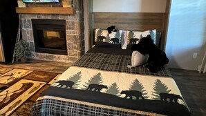 A cozy room with a stone fireplace, a television mounted on the wall, and a bed with a forest-themed bedspread. - Cozy Riverside Studio in the Heart of Townsend (Townsend)