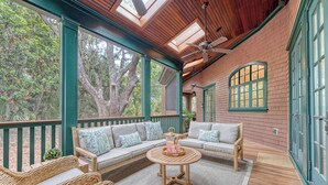 A covered outdoor seating area with wicker furniture, a round table, and a ceiling fan.