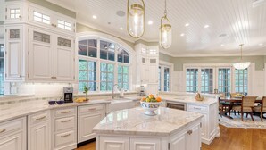 A spacious kitchen with white cabinetry, a large island, and a dining area with a wooden table and chairs.