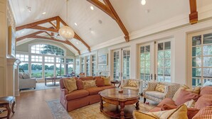 A spacious living room with a high ceiling, large windows, and a fireplace.
