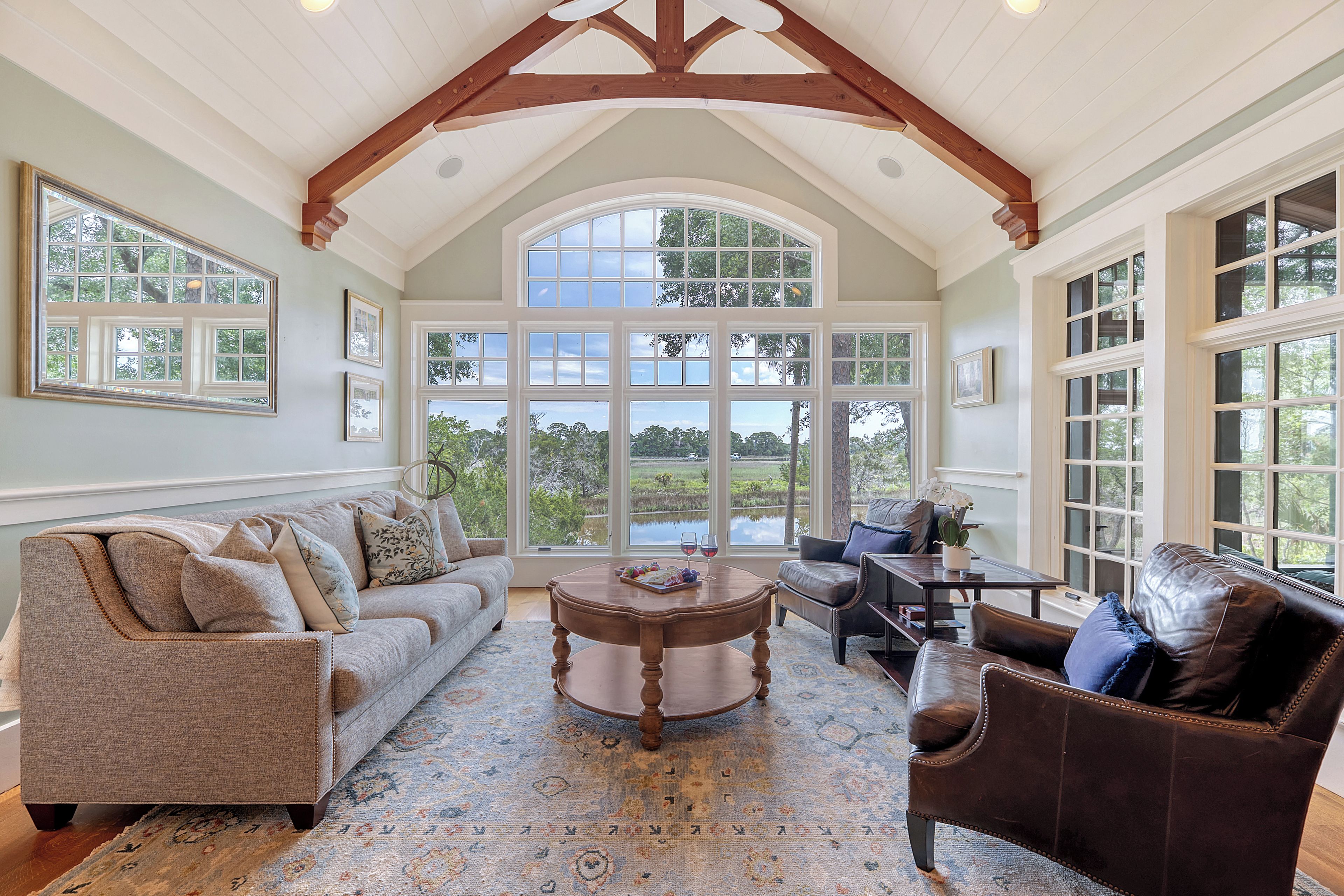 A spacious living room with a high ceiling, large windows, and a view of greenery outside.