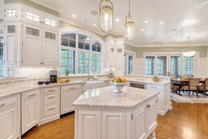 A spacious kitchen with white cabinetry, a large island, and a dining area with a wooden table and chairs. - River views, guest house and pool (Kiawah Island)